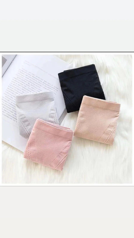 Three pairs of underwear in black, pink, and beige on a white surface with a book.